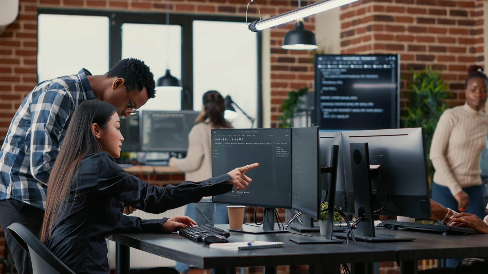 A diverse team of professionals working in an office setting, collaborating on data tasks at multiple computer workstations, with code displayed on monitors and a modern workspace environment.