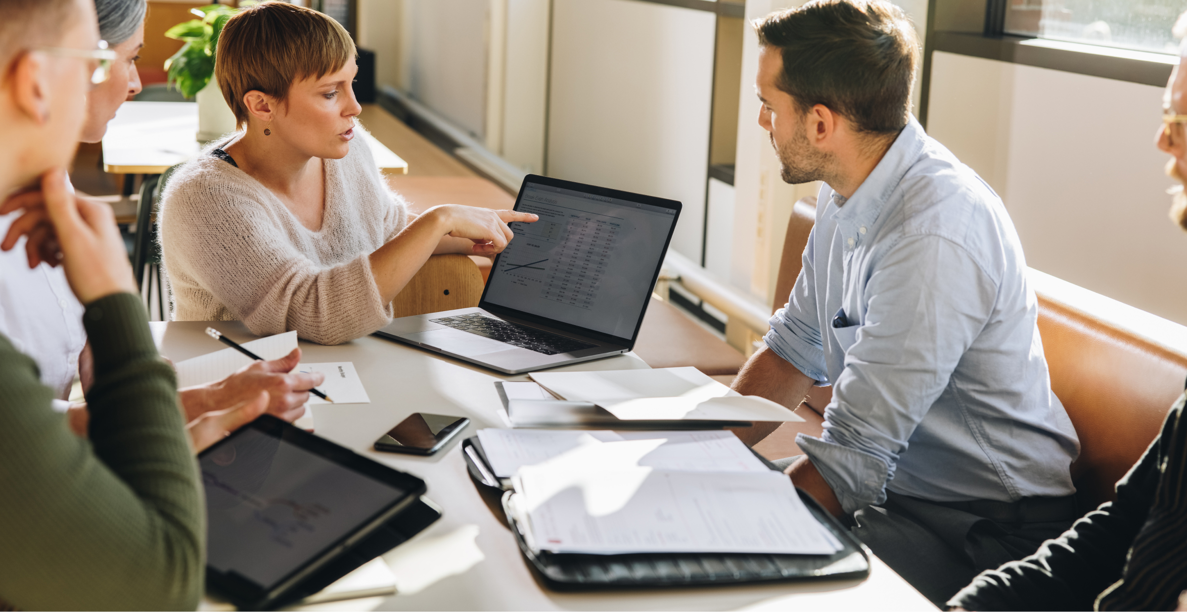 A group of five people is engaged in a discussion around a table with laptops