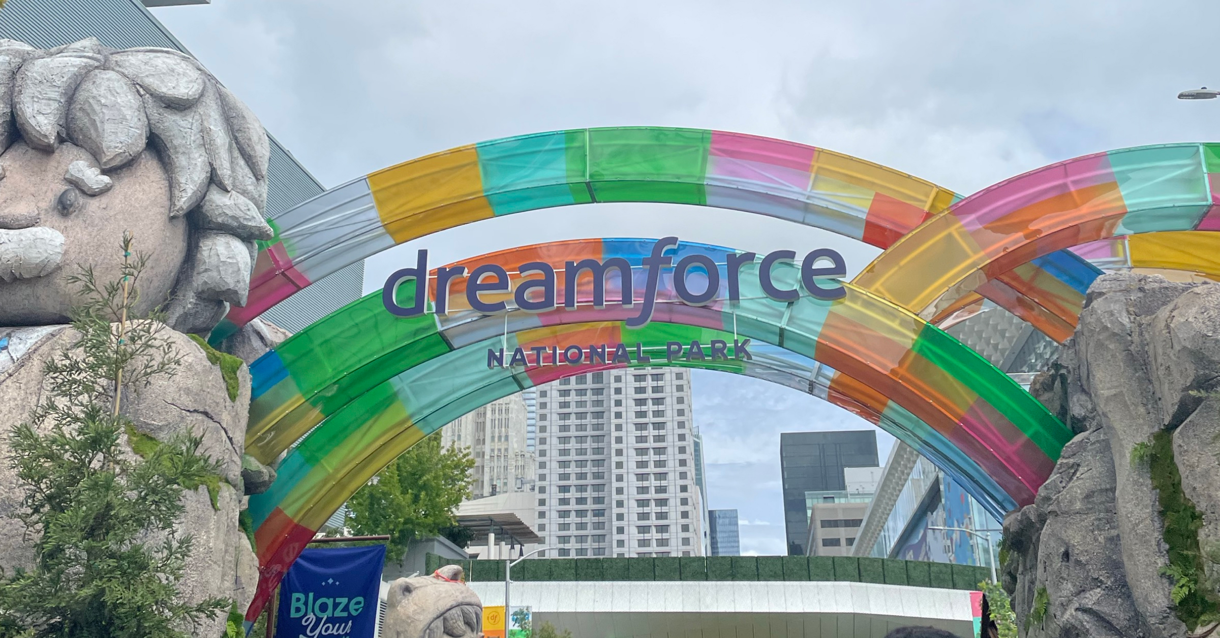 Colorful arches at the entrance of Dreamforce 2024 National Park, with a large stone statue and vibrant decorations set against a cityscape backdrop.