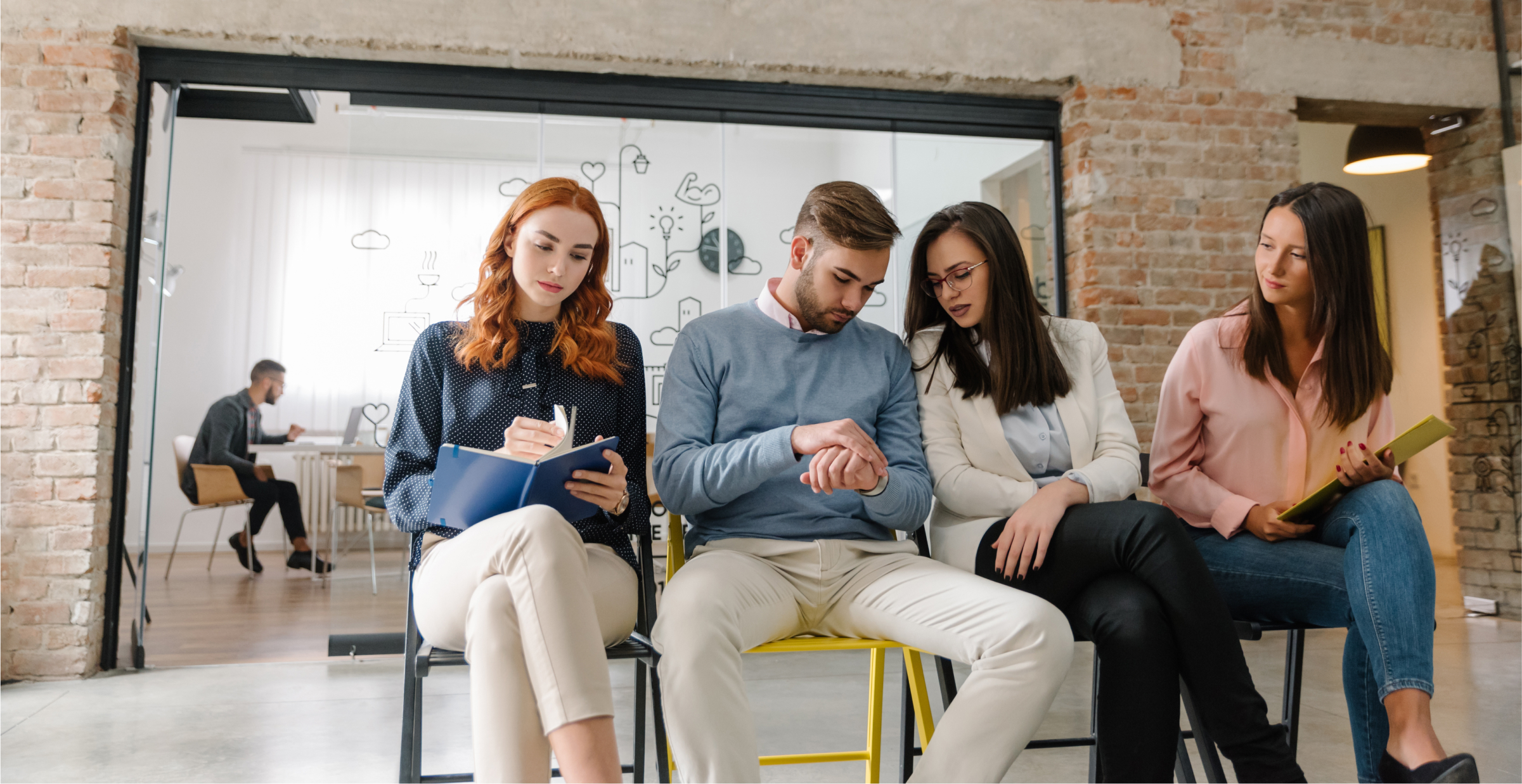 Four people seated in a row, with one man checking his watch. A person is working in the background behind a glass partition.
