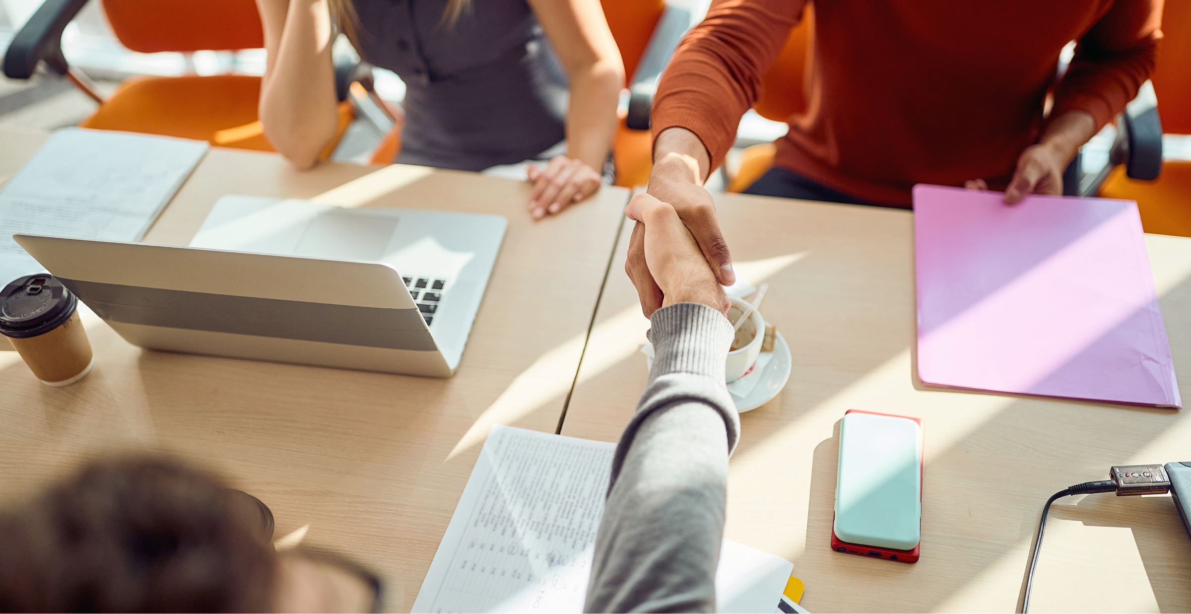 Two individuals shaking hands at a meeting table, symbolizing agreement and collaboration in a professional setting.