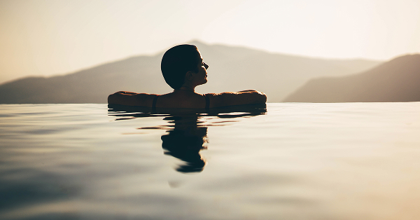 A woman wading in the water during a vibrant sunset, with warm colors reflecting on the surface