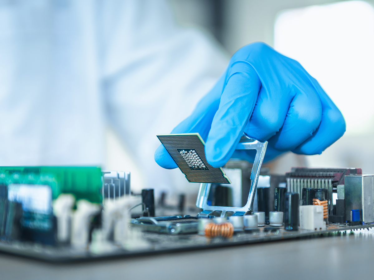 Gloved hand holding a CPU chip above a motherboard socket ready for installation during hardware assembly.
