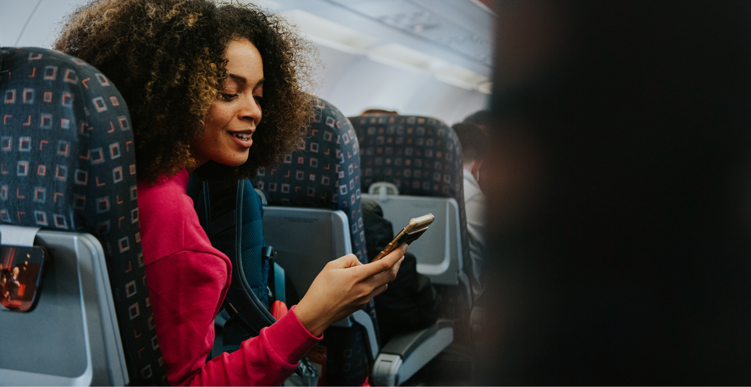 A woman sitting on an airplane, focused on her phone while enjoying her flight