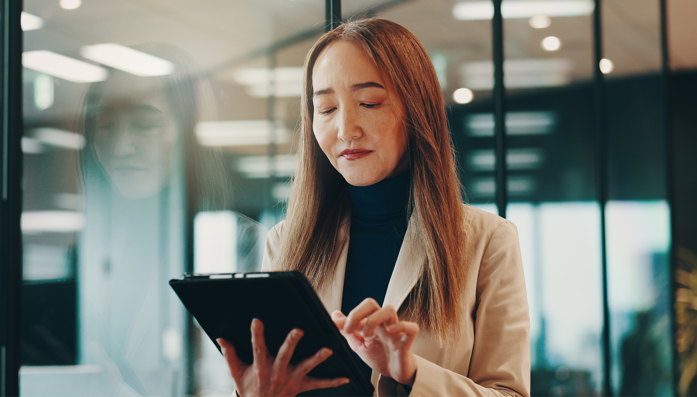 A woman in a business suit holds a tablet, appearing focused and engaged in a professional setting.  