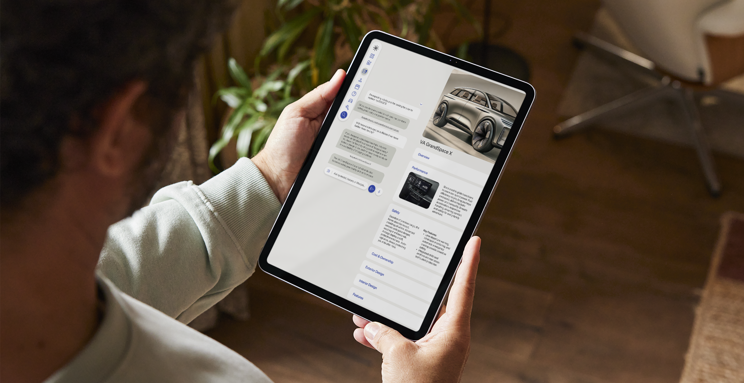 Person holding a tablet while browsing a car information app, displaying details and images of the VA GrandSpace X SUV.