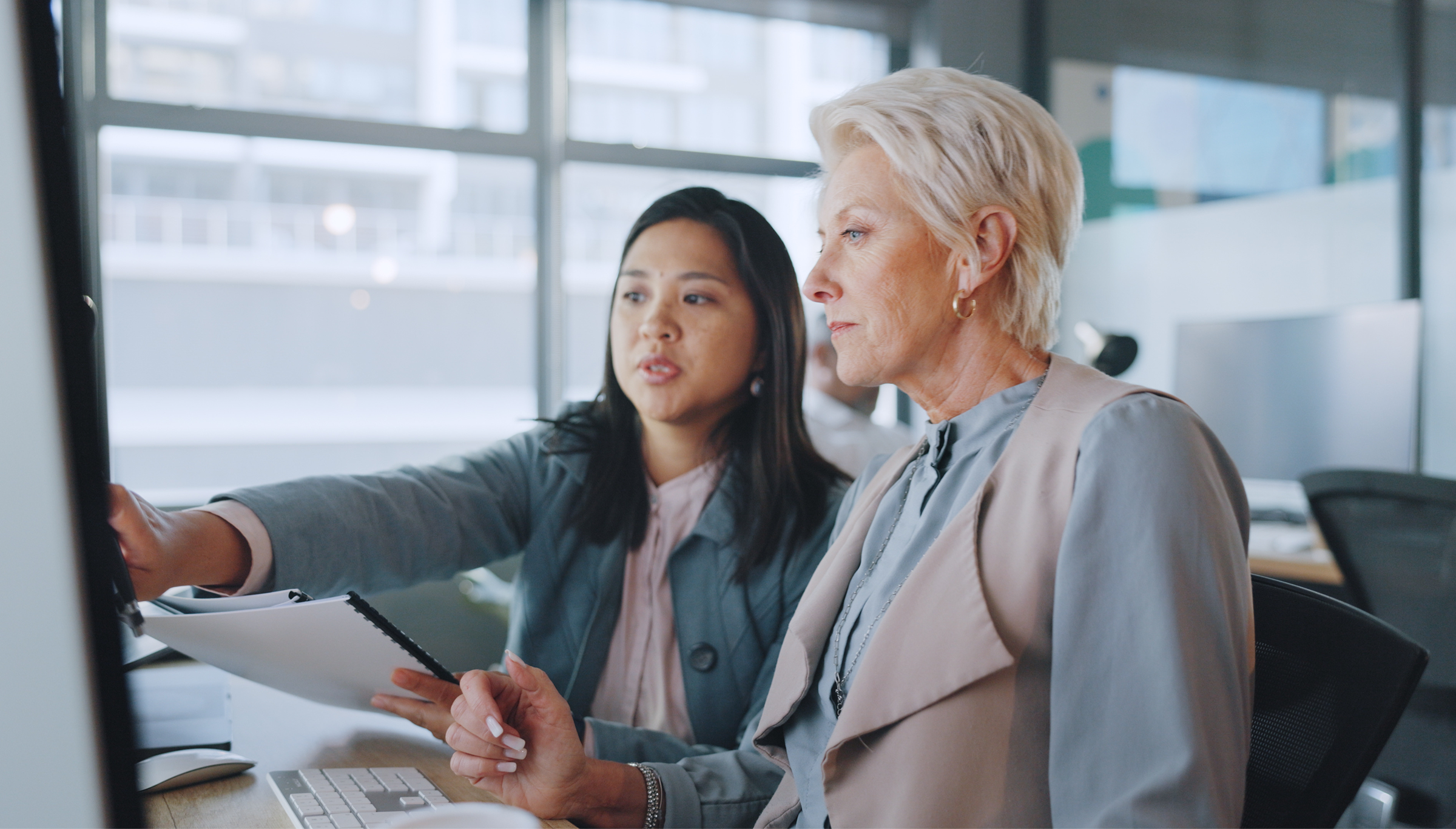 Two professional women reviewing data on a computer screen in a modern office, highlighting teamwork and digital business strategy.