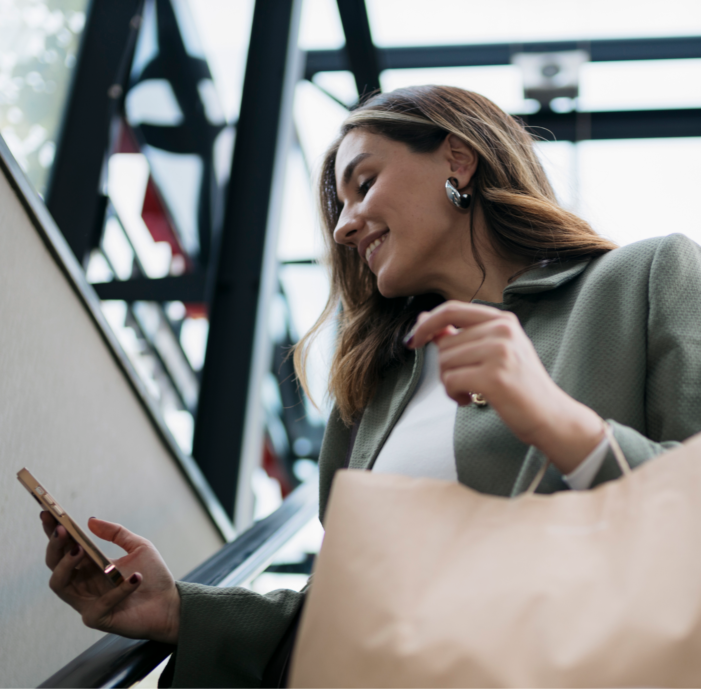 A woman holds a shopping bag while looking at her phone, appearing engaged in a mobile activity.  
