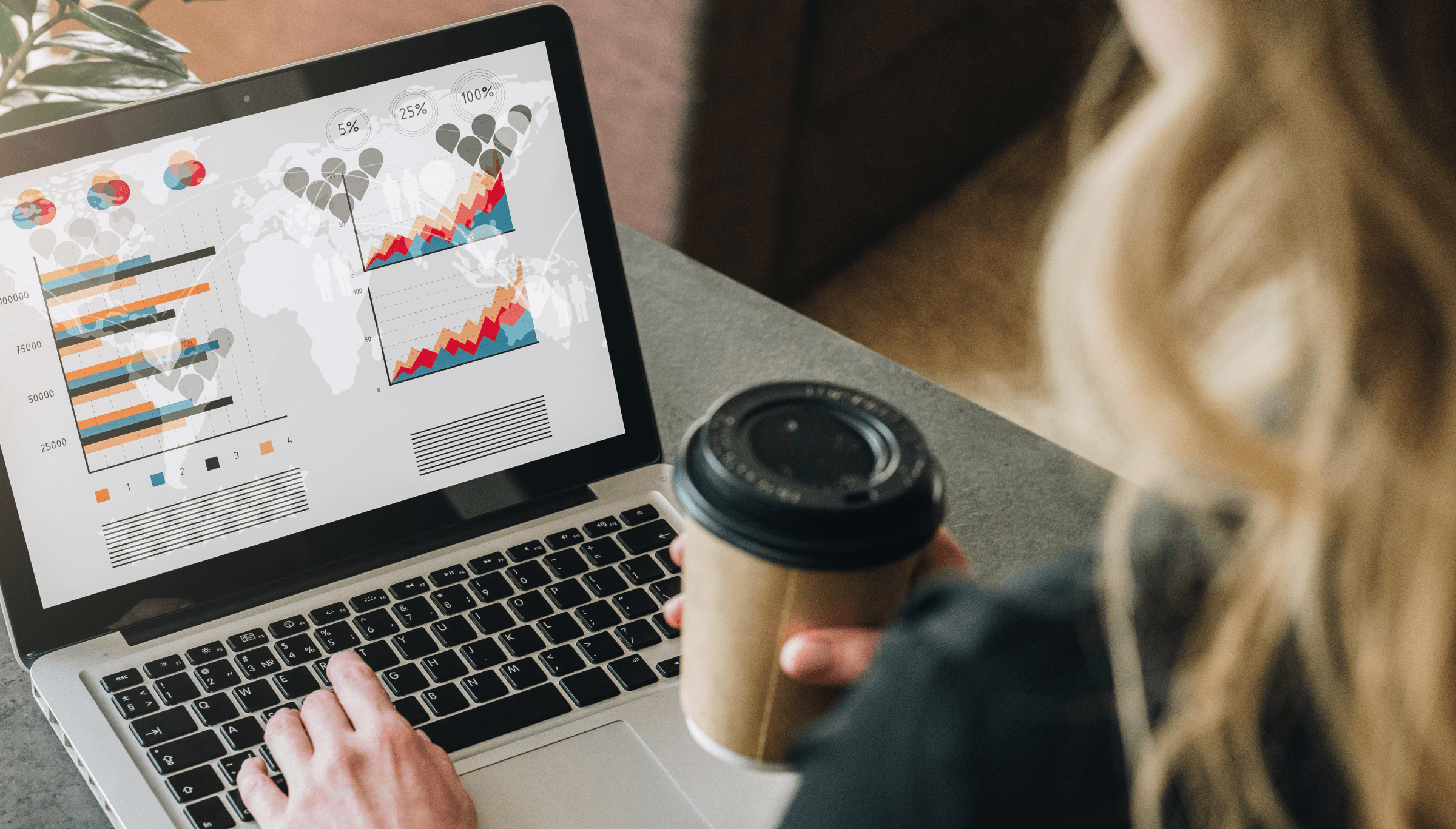 A person is analyzing data on a laptop while holding a coffee cup in one hand. The laptop screen displays various graphs and charts, including bar charts and line graphs, against a backdrop of a world map. The charts show data trends and percentages, suggesting a focus on global analytics or market research. The setting is casual, with the person seated at a desk or table, engaging in work or study with a focus on data analysis.