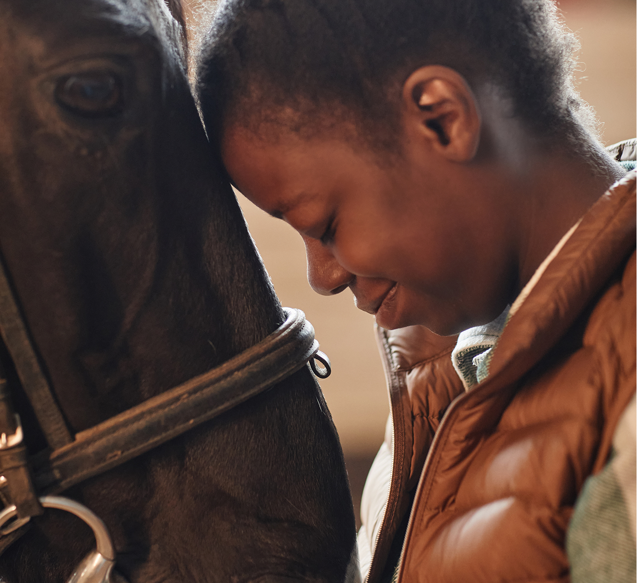 A young girl gently pets a brown horse, smiling as she interacts with the animal in a sunny outdoor setting.  