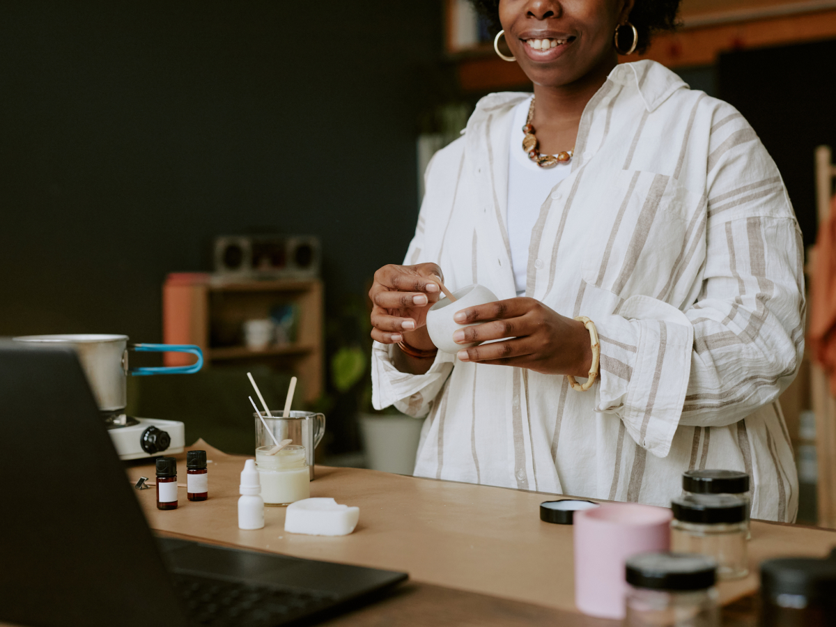  A woman is smiling as she works on making a candle. 