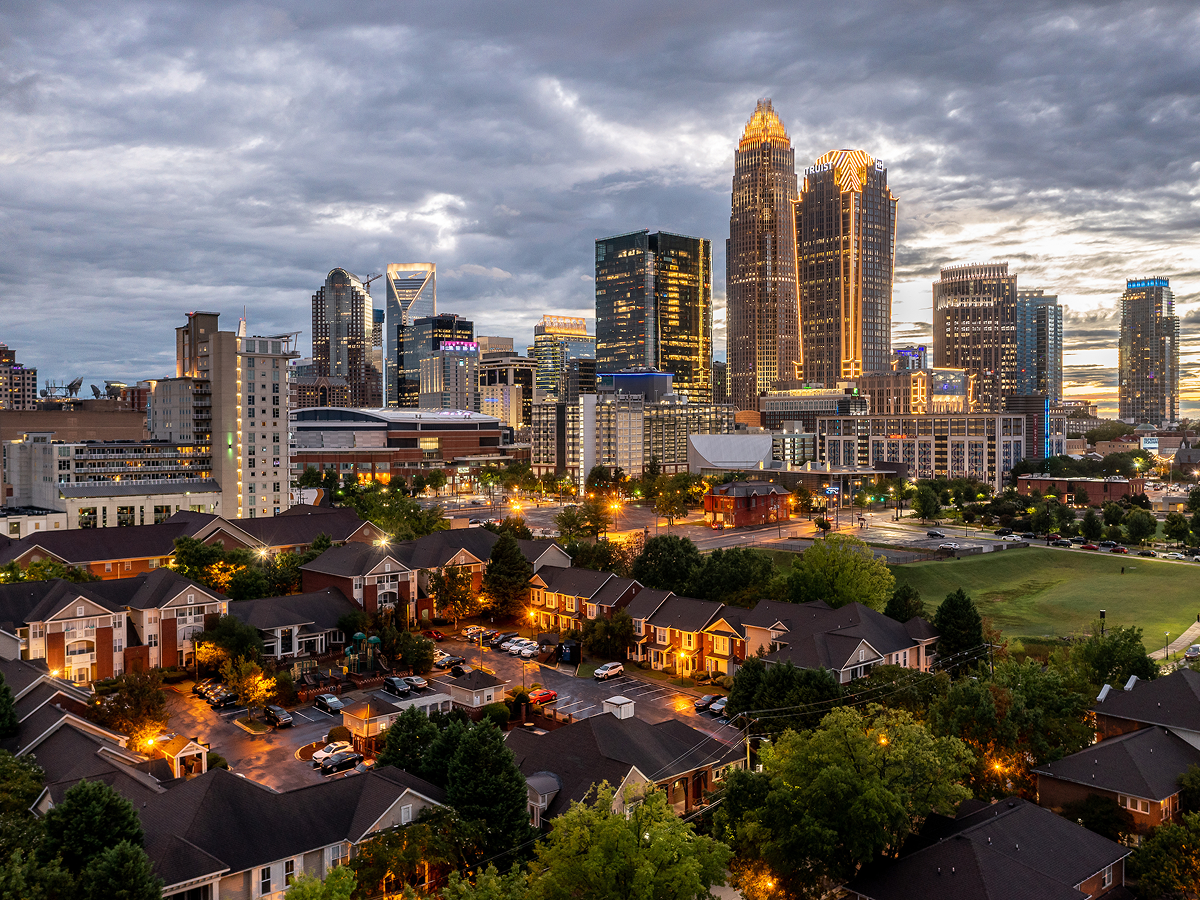 Evening view of Charlotte, North Carolina skyline with illuminated buildings and nearby residential neighborhood, highlighting urban tourism appeal.
