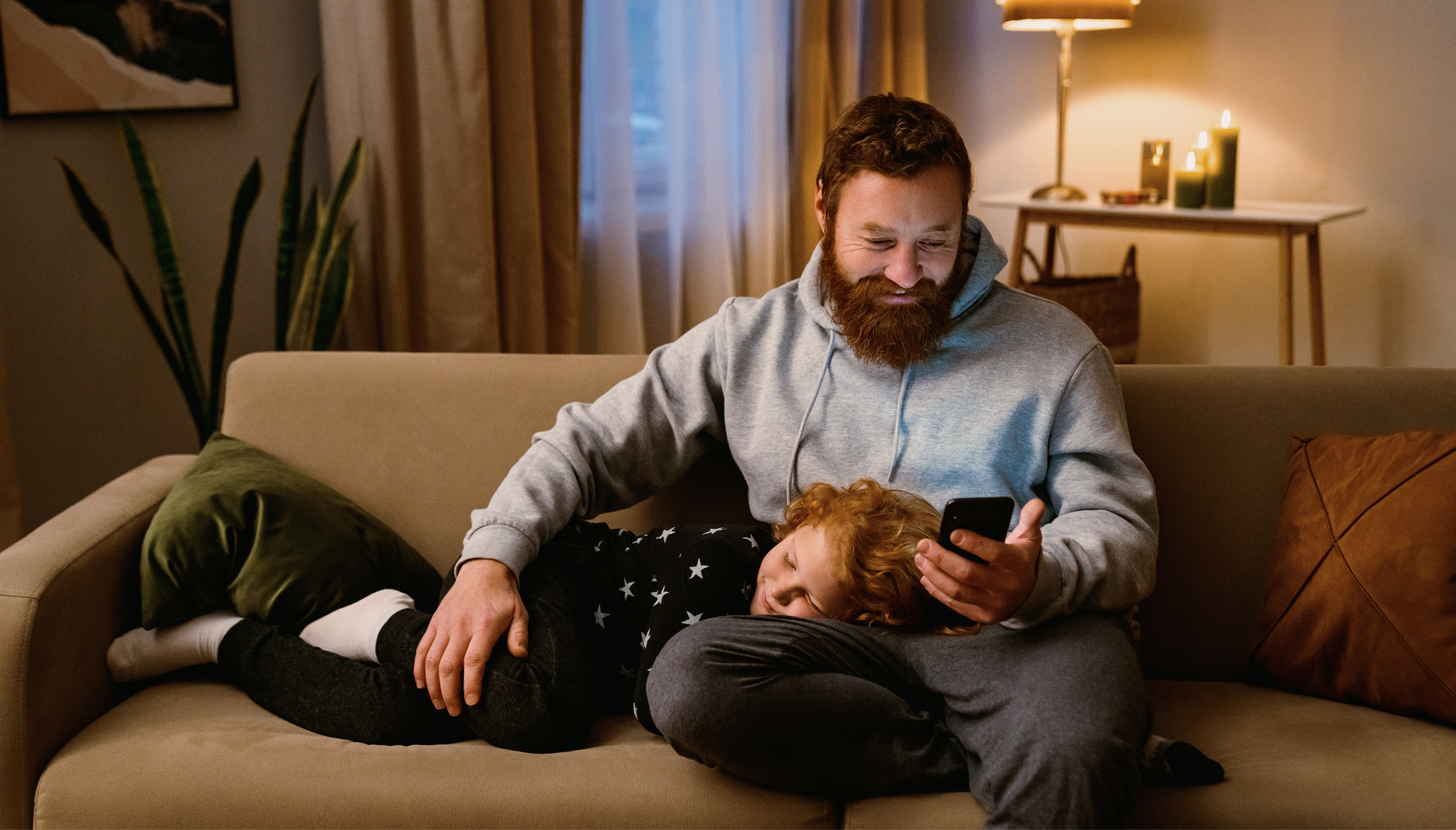 A man and a child sit together on a couch, looking at a phone and sharing a moment of connection