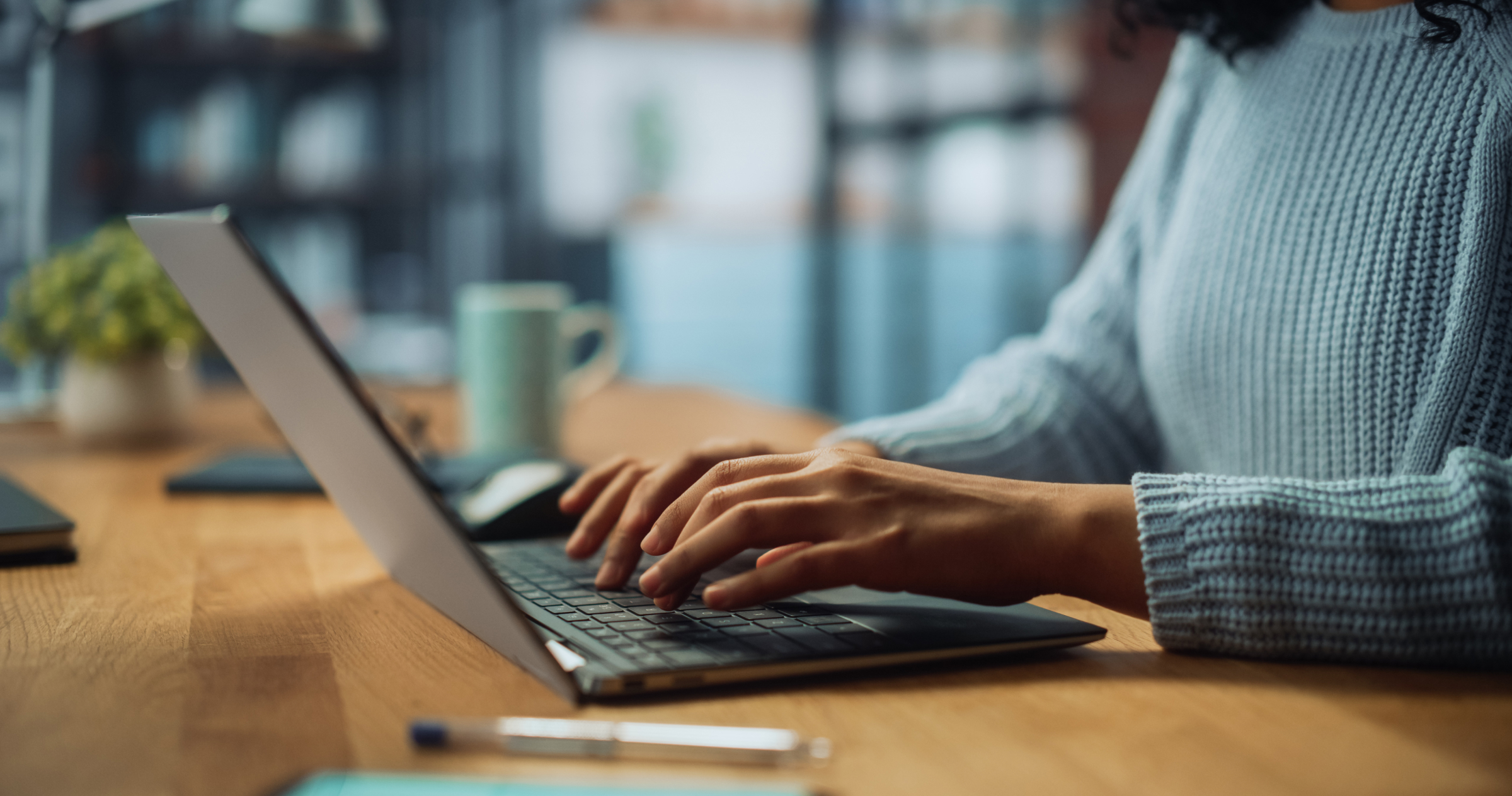 Close image of a woman in a blue sweater as her hands are typing on a laptop keyboard.