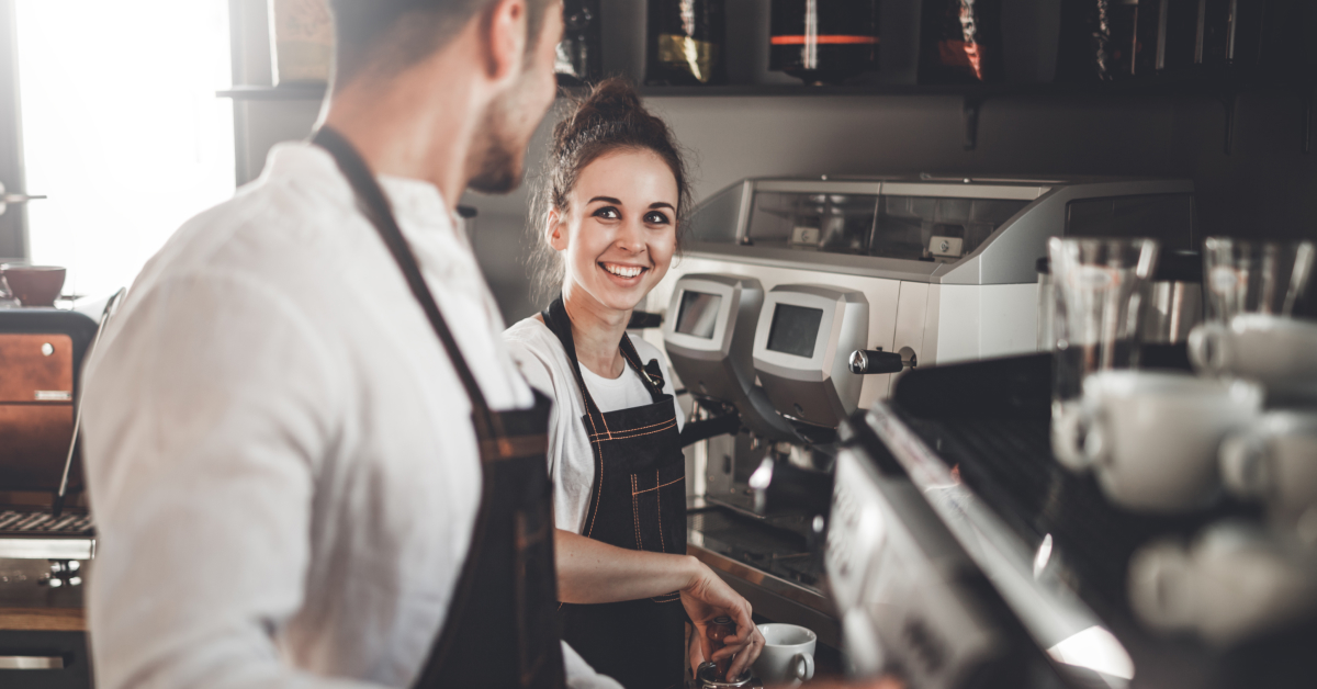 A cheerful man and woman collaborate in a coffee shop, showcasing teamwork and a friendly atmosphere.
