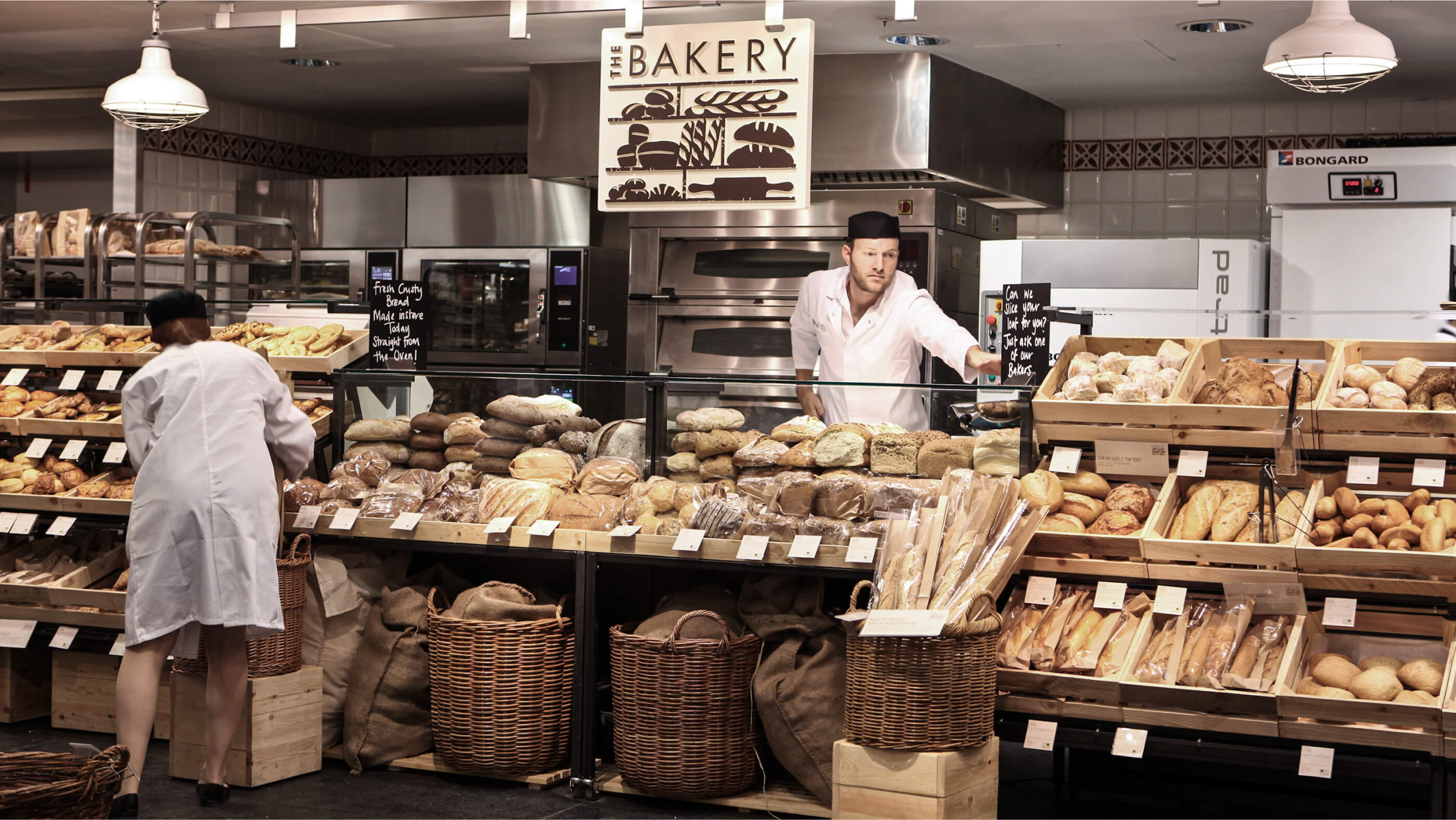 Two bakery workers are busy in a well-stocked bakery. 