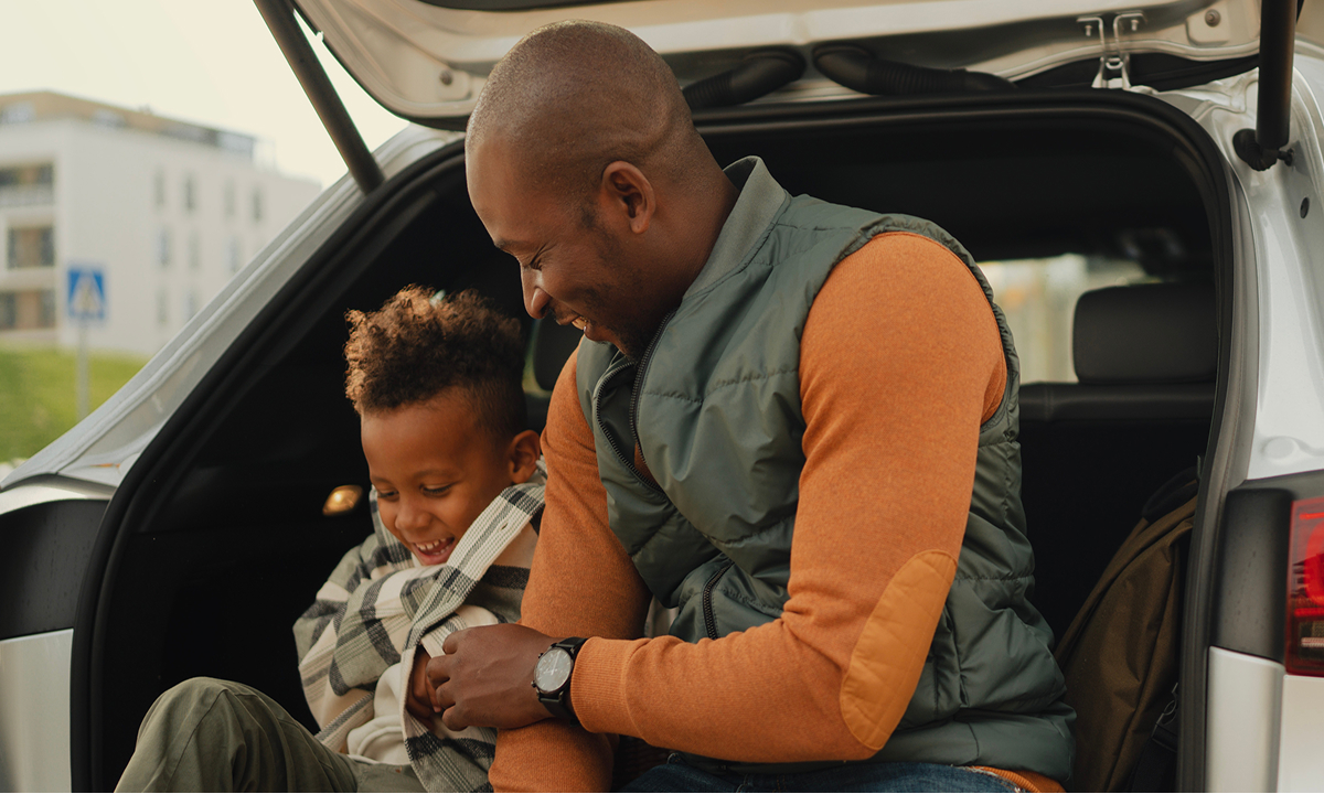 A man and a child sitting together in the open trunk of a parked car, enjoying a moment outdoors.