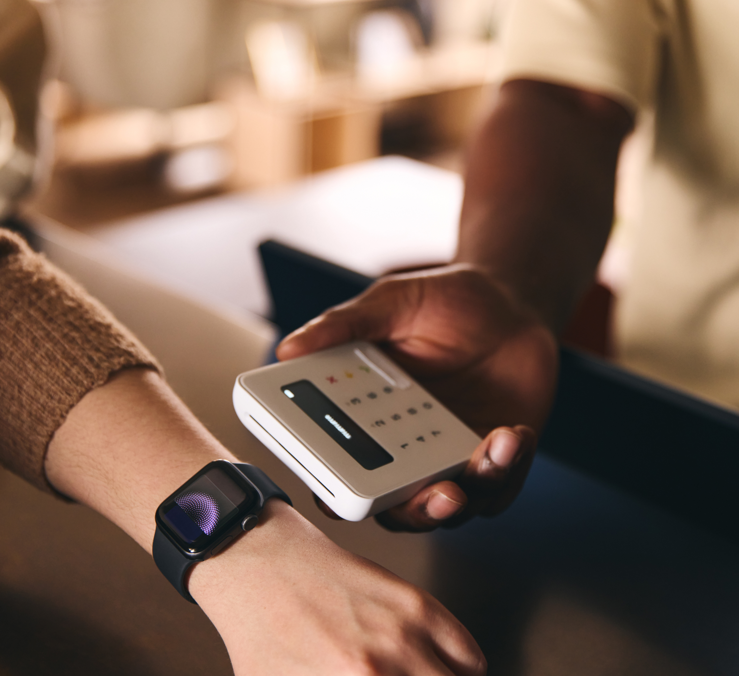 A person using a smartwatch to make a contactless payment while another person holds a card reader.