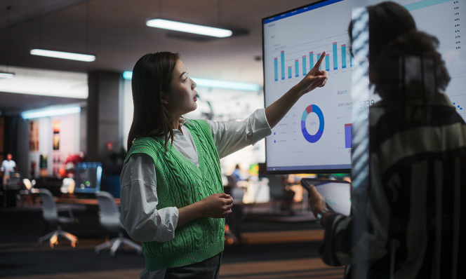 Female retail analyst presenting predictive analytics on a large digital screen, highlighting data-driven decision-making and immersive retail innovation.