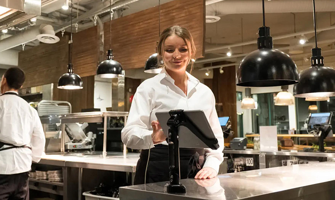 Restaurant staff member using a touchscreen POS system in a modern kitchen environment, showcasing agile retail and hospitality technology.