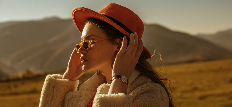 Fashionable woman in an orange hat and sunglasses standing outdoors in natural light, showcasing fall fashion and seasonal apparel trends.