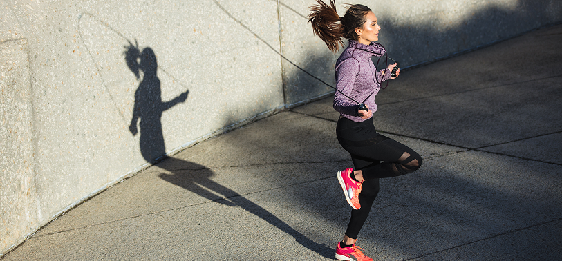 Athletic woman in fitness apparel jumping rope on an outdoor pavement, showcasing active lifestyle, sportswear, and outdoor exercise.