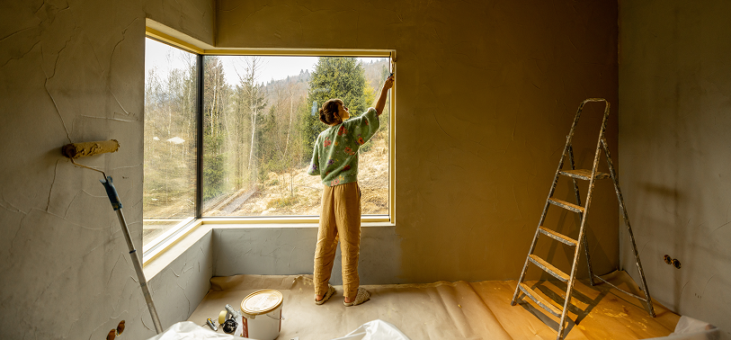 Woman painting a window frame in a sunlit room during a home improvement project, featuring DIY renovation and interior design updates.
