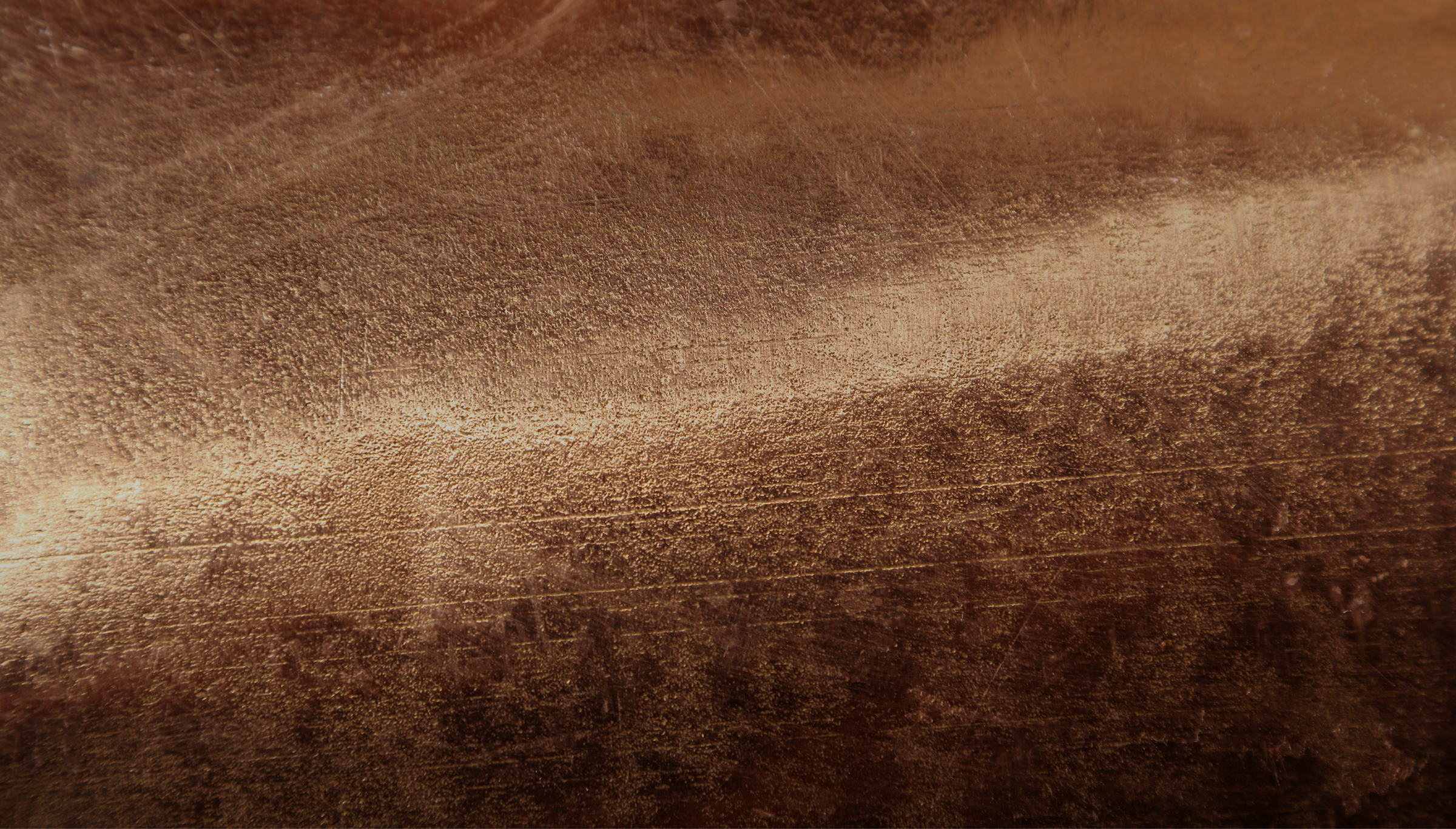 Close-up of a brushed bronze metallic surface with textured details and natural light reflections, ideal as a background for design or branding.
