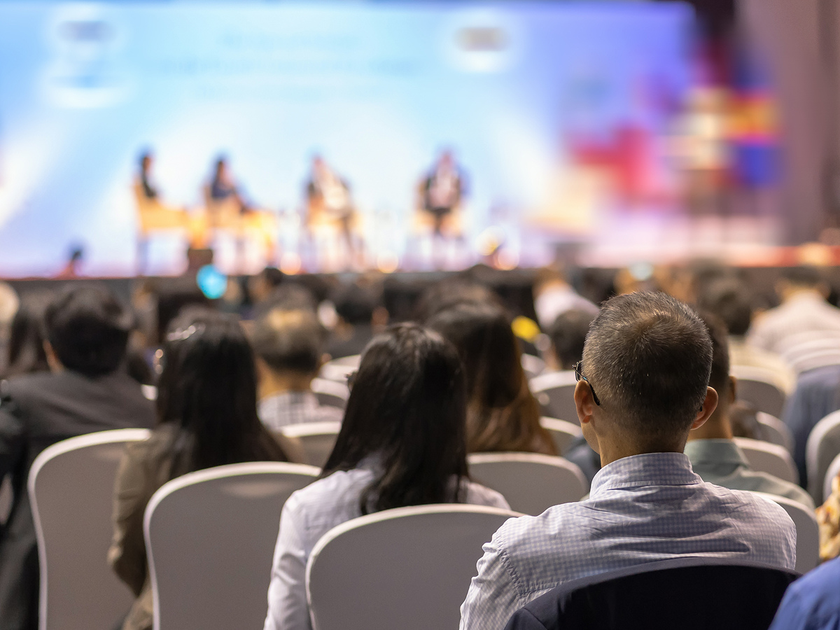 A large crowd of people seated in chairs, attentively listening at a conference event.  