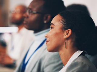 A woman sits among a group of people, looking engaged in the conversation around her.
